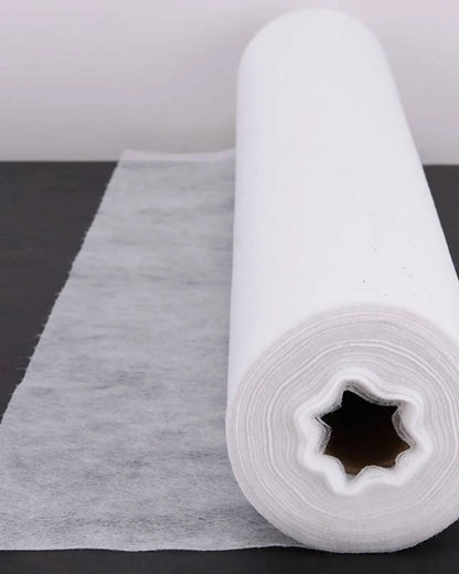 White disposable medical bed sheet roll on black table, unrolled for home care use