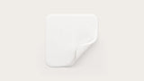 Sterile white adhesive medical wound dressing pad with rounded corners on neutral background