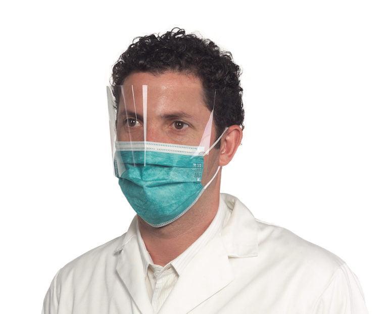 Man wearing teal surgical mask with attached clear face shield, white lab coat, medical PPE