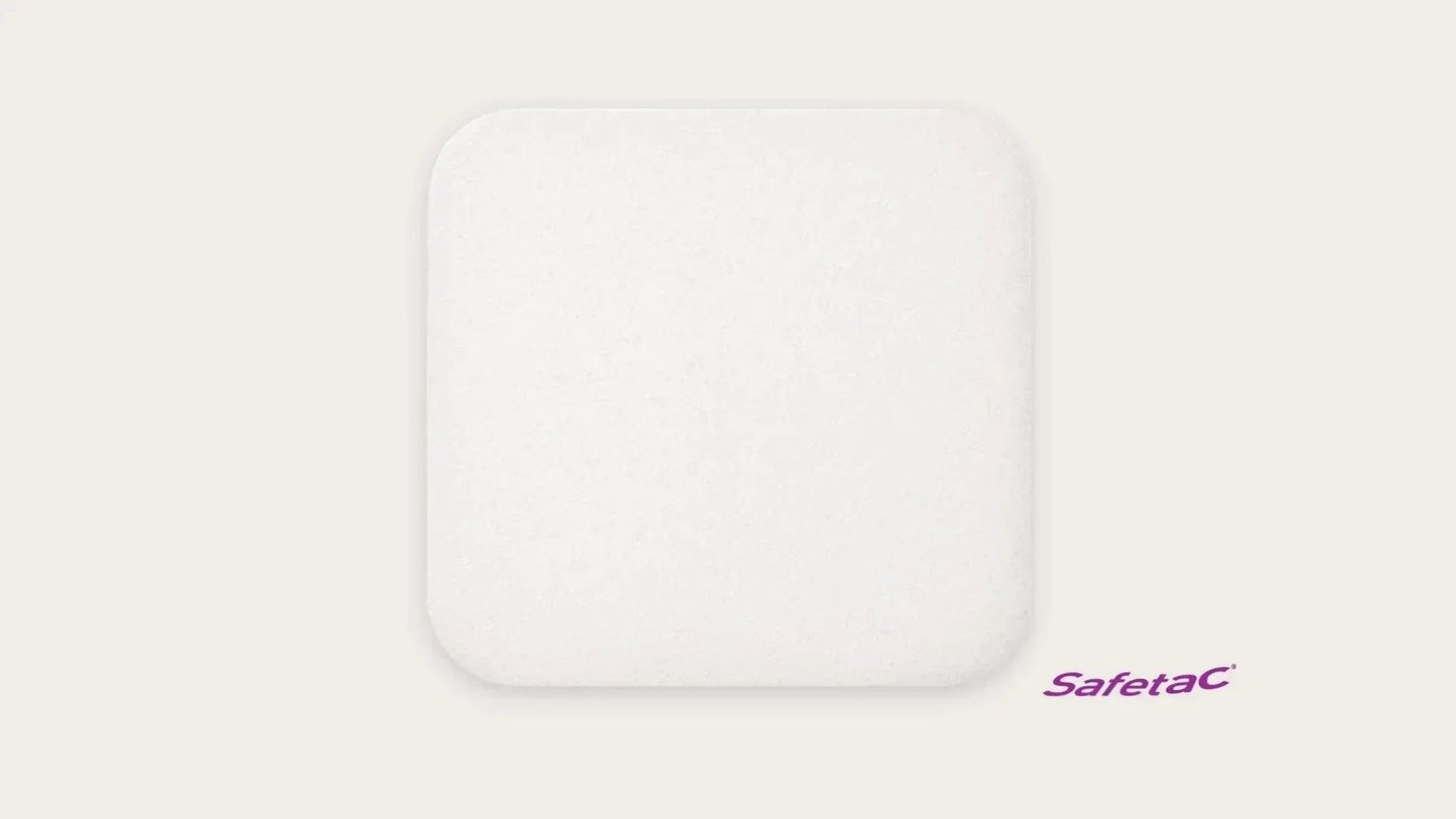 Square white foam medical dressing pad with rounded corners on a plain background, Safetac logo visible