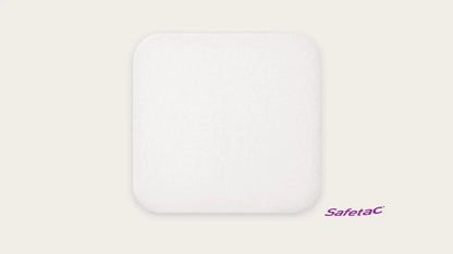 Square white foam wound dressing with rounded corners on a beige background, Safetac logo visible.