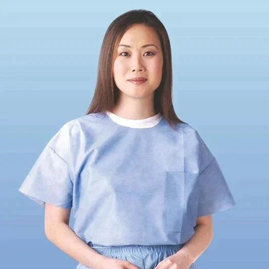 Woman wearing disposable medical gown, standing against a blue background