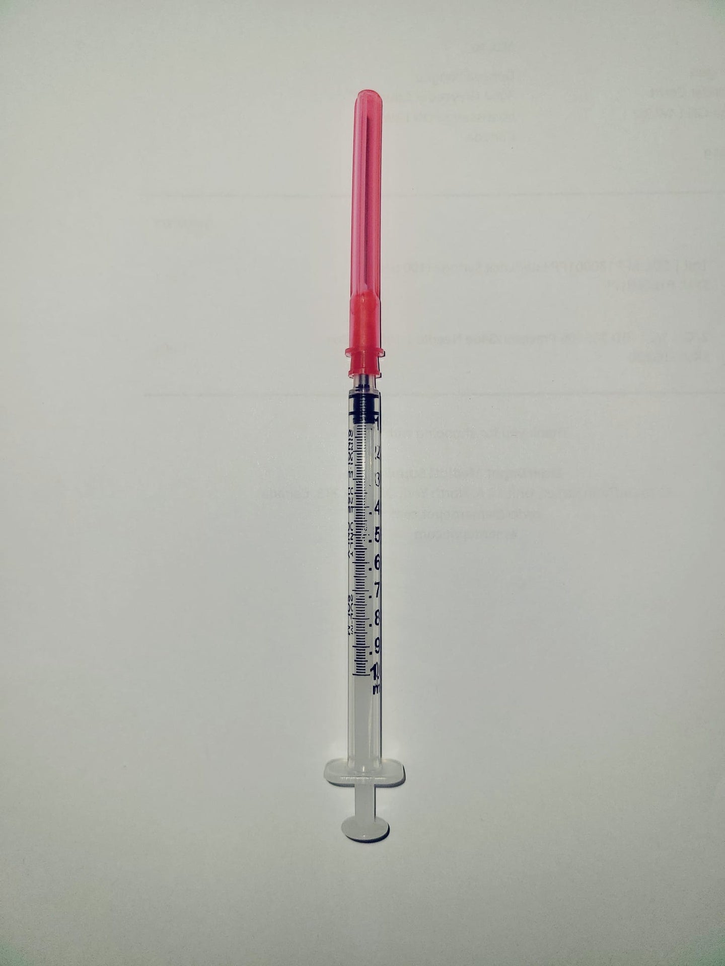 Medical syringe with clear barrel and red needle cap on white background