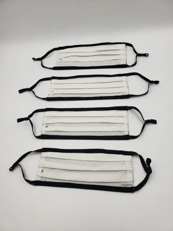Four pleated white cotton face masks with black ear loops in various sizes on a white background.